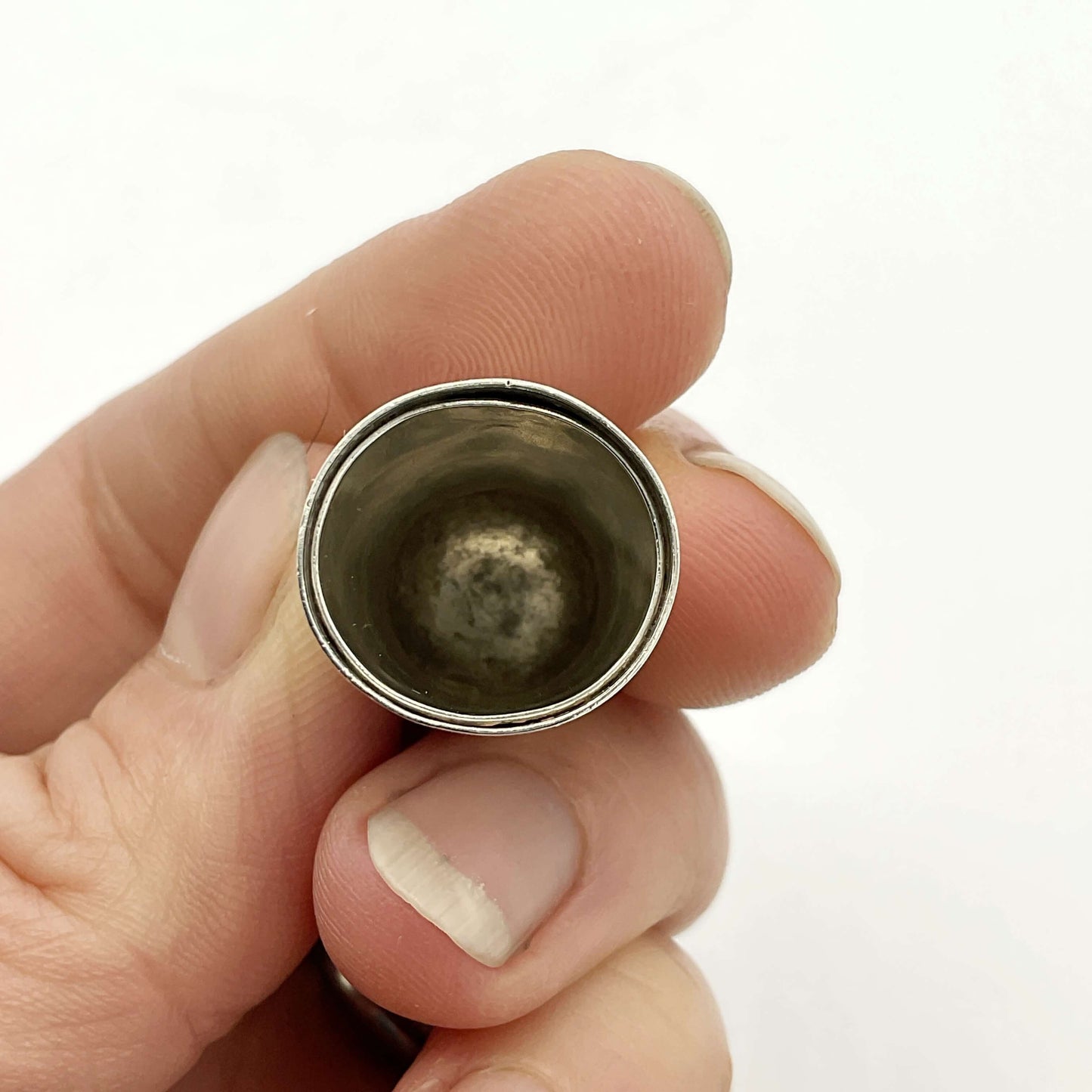Hand holding a thimble showing the inside against a white background