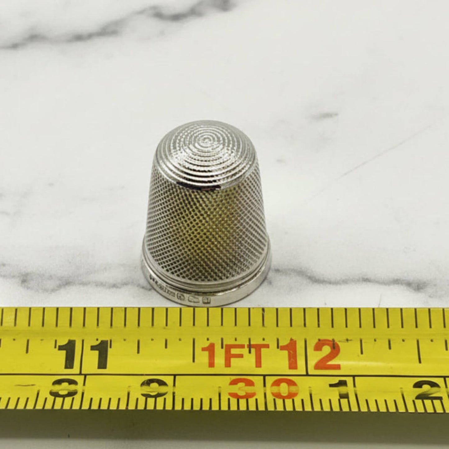 Silver thimble on a marble surface with a measuring tape for scale.