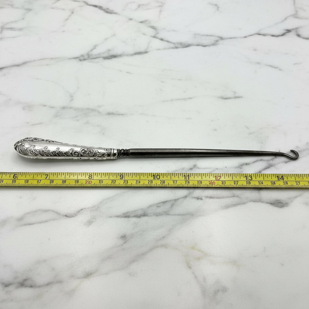 silver button hook next to tape measure showing length as 23cm