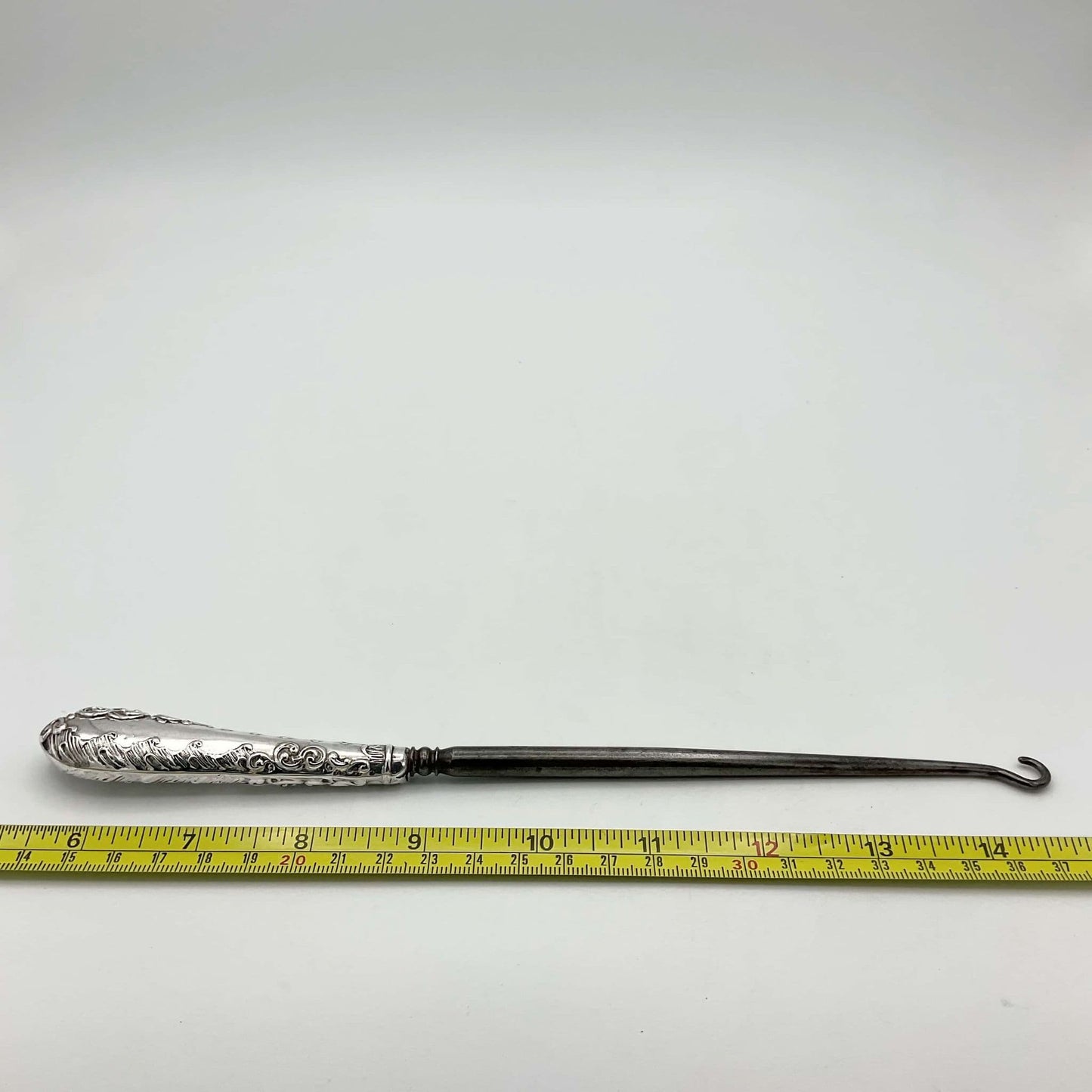 silver button hook next to tape measure showing length as 23cm
