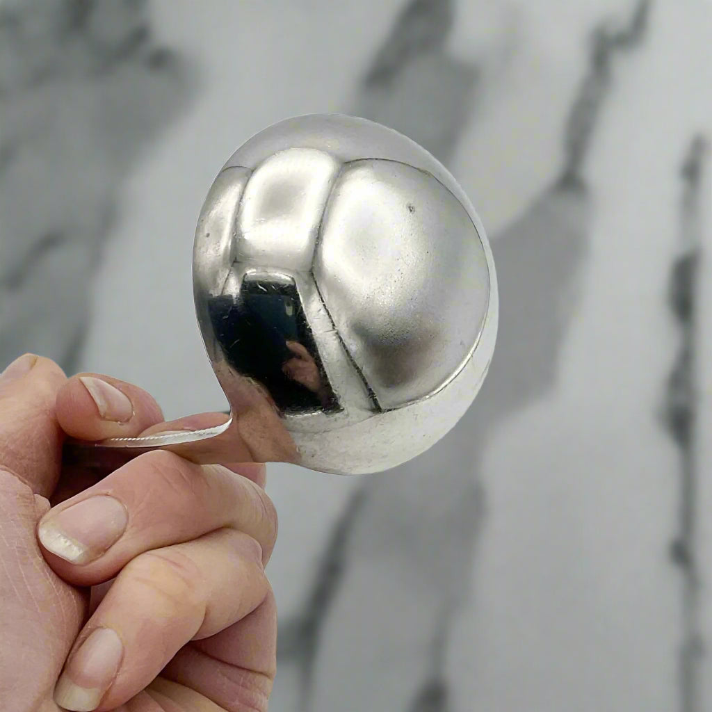 Hand holding a a back  of a silver ladle against a marble background