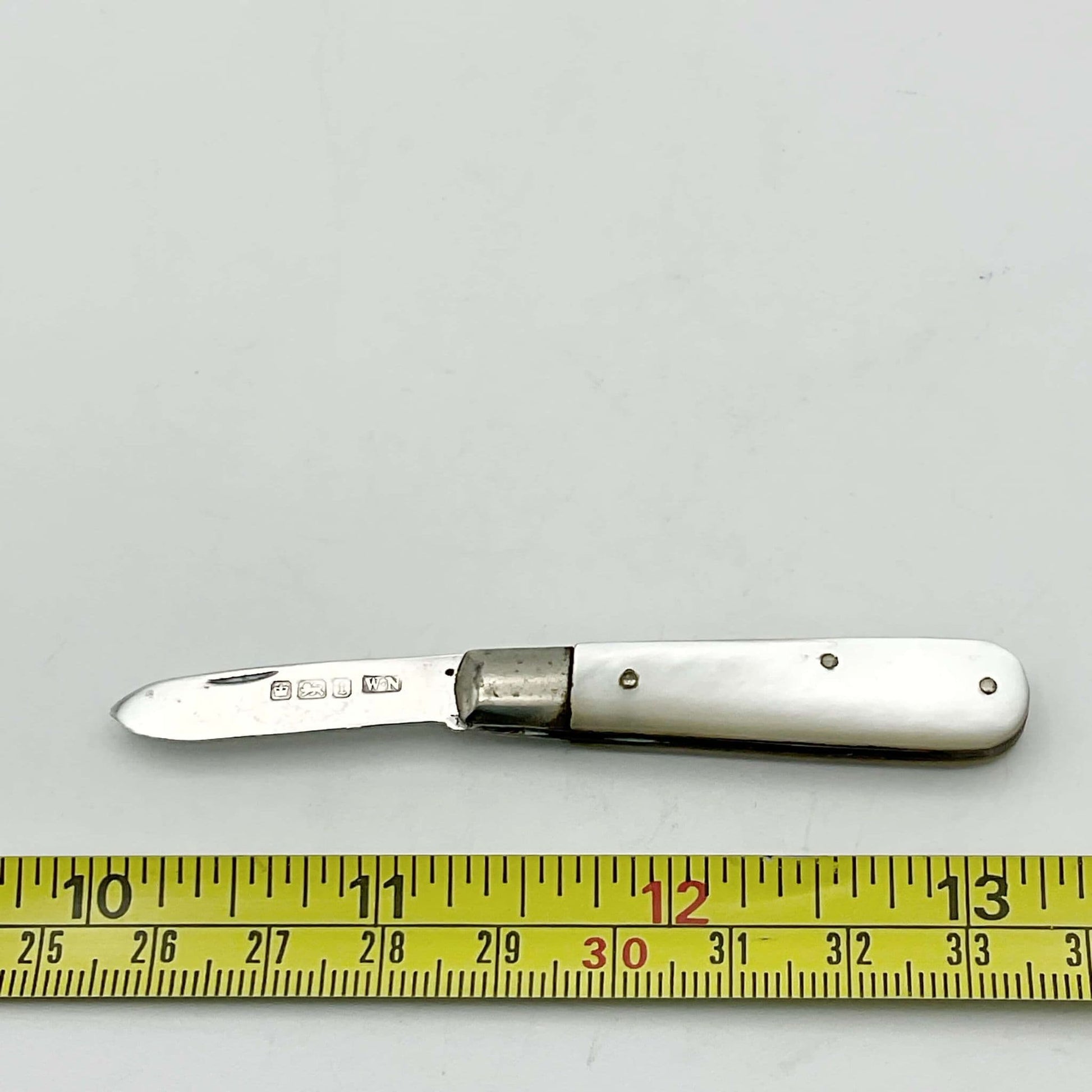 Silver fruit knife with a mother of pearl handle on a white background next to a tape measure, showing the length as approximately 9cm