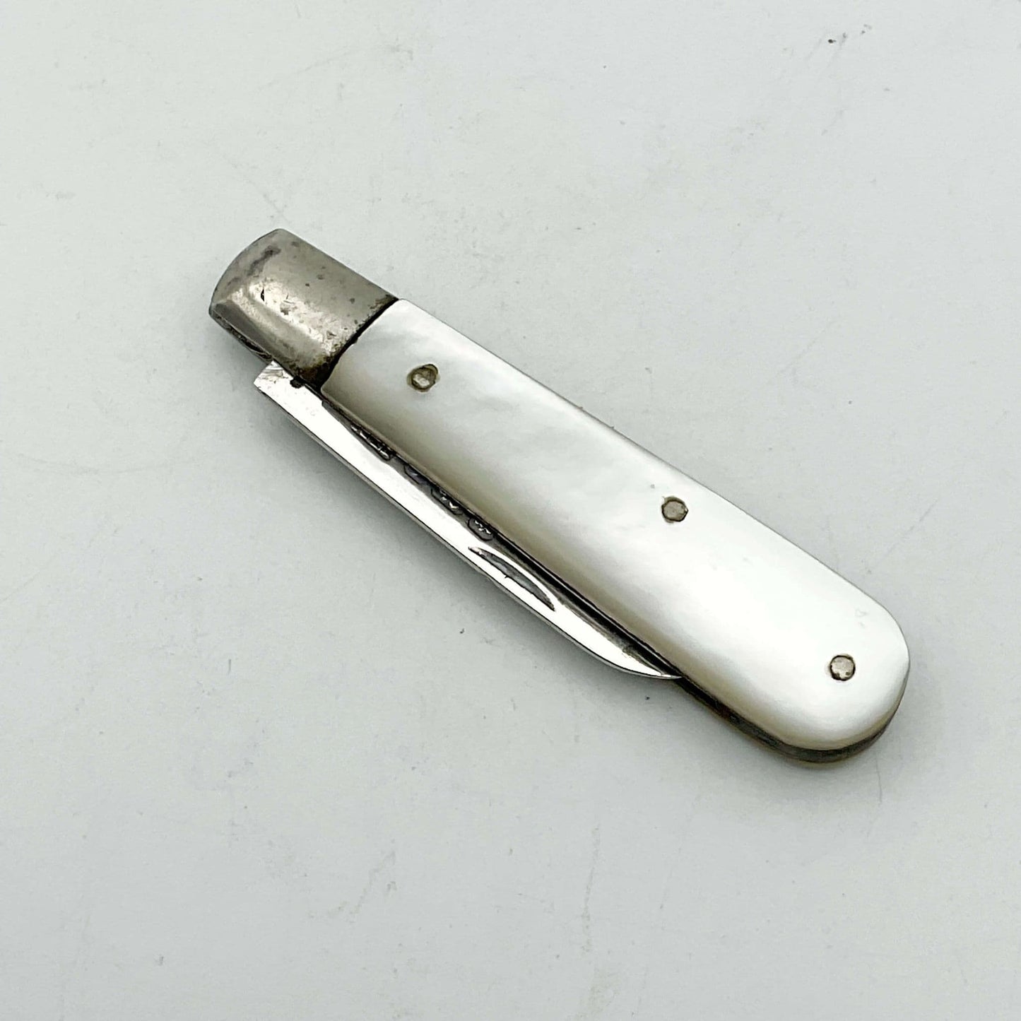 Silver fruit knife with a mother of pearl handle with the blade folded away on a white background