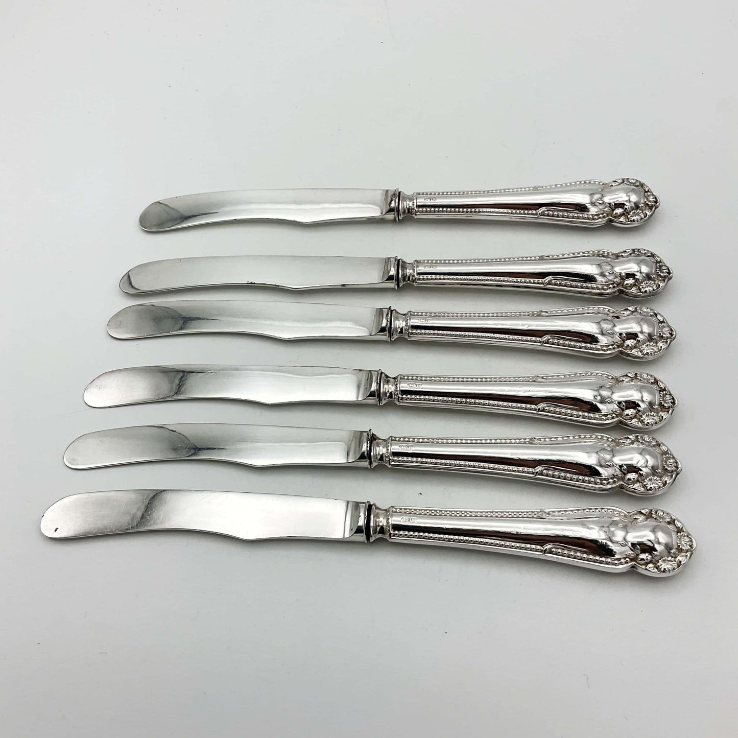 Six antique silver tea knives on a plain background