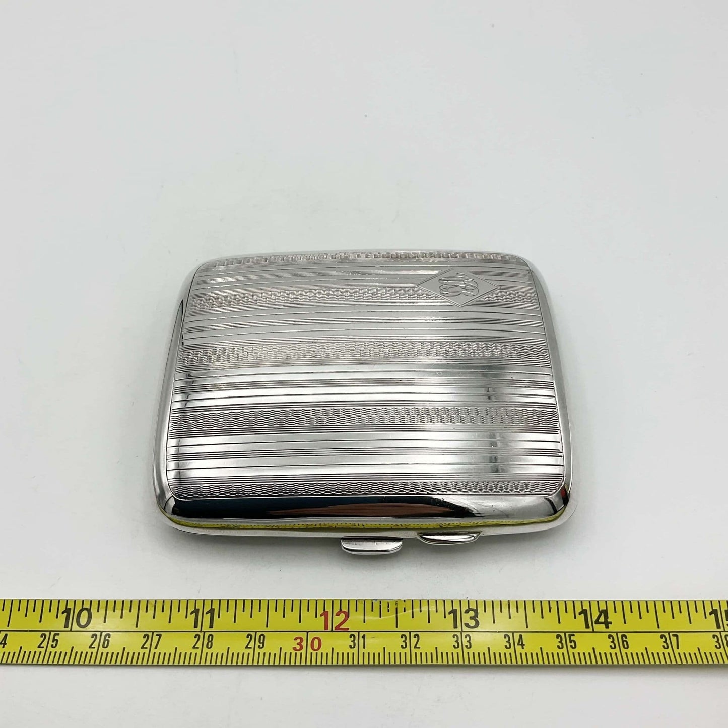 Antique silver cigarette case next to a tape measure showing it's height as 9cm