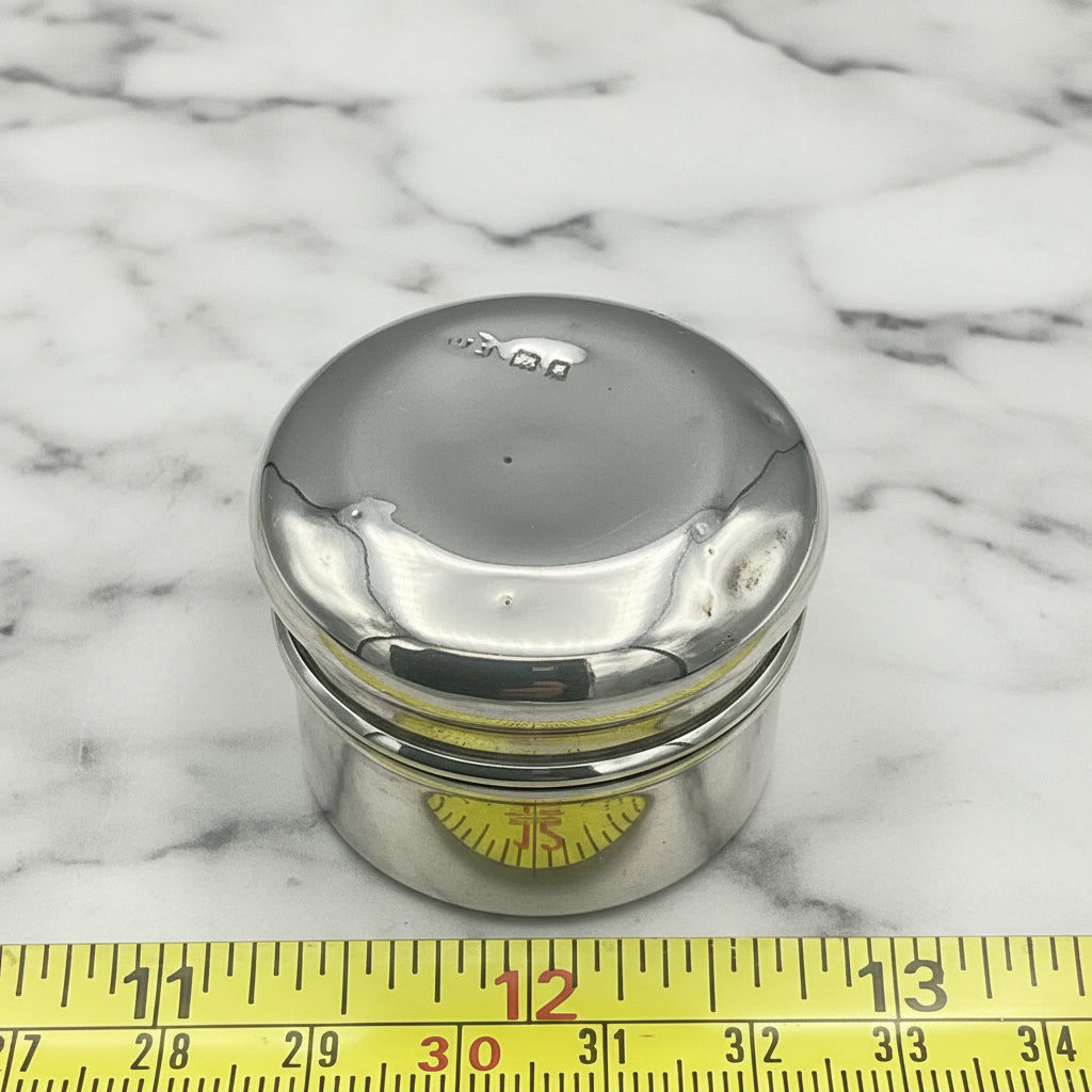silver pot next to tape measure for scale on a marble surface