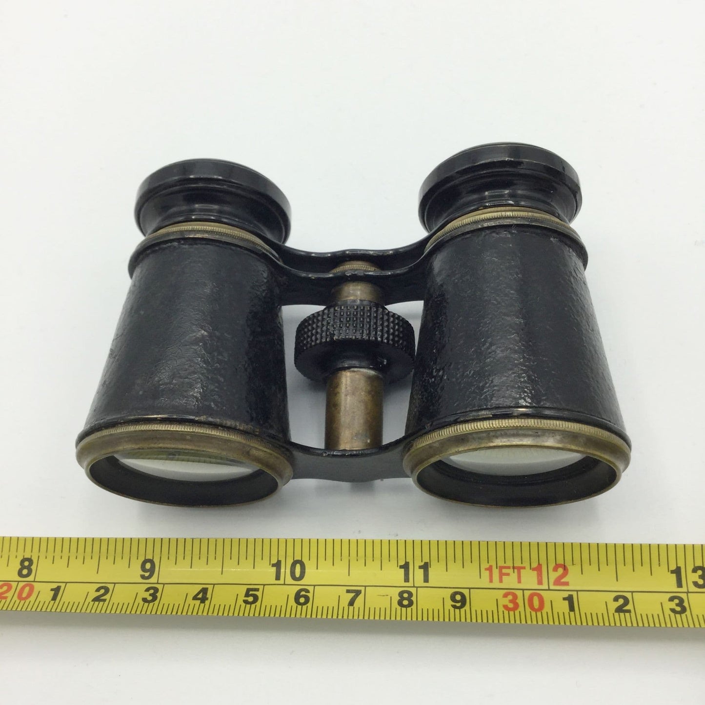 antique black binoculars on a marble surface next to a tape measure for scale