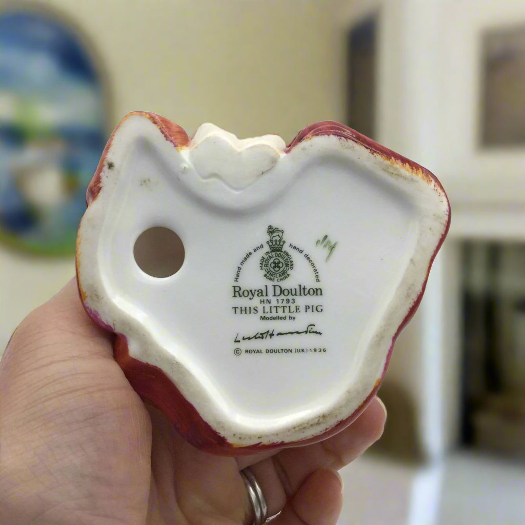 base of Royal Doulton This Little Pig ornament held in a hand in a room