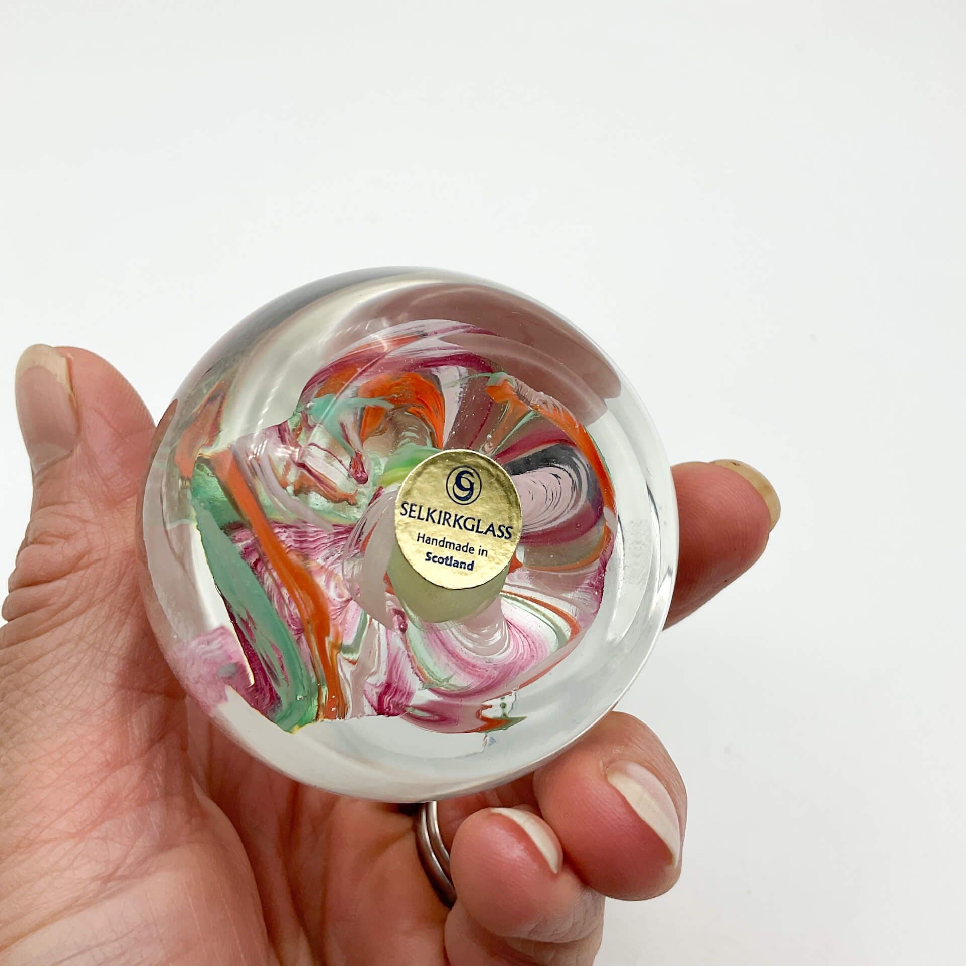 Base of Selkirk glass paperweighrt with multicoloured swirls held of a hand on a white background.