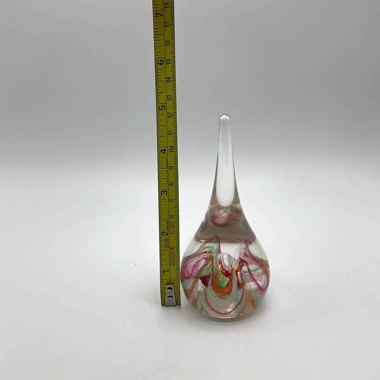 Selkirk glass paperweighrt with multicoloured swirls on a white background next to a tape measure showing the height asc just under v5 inches.