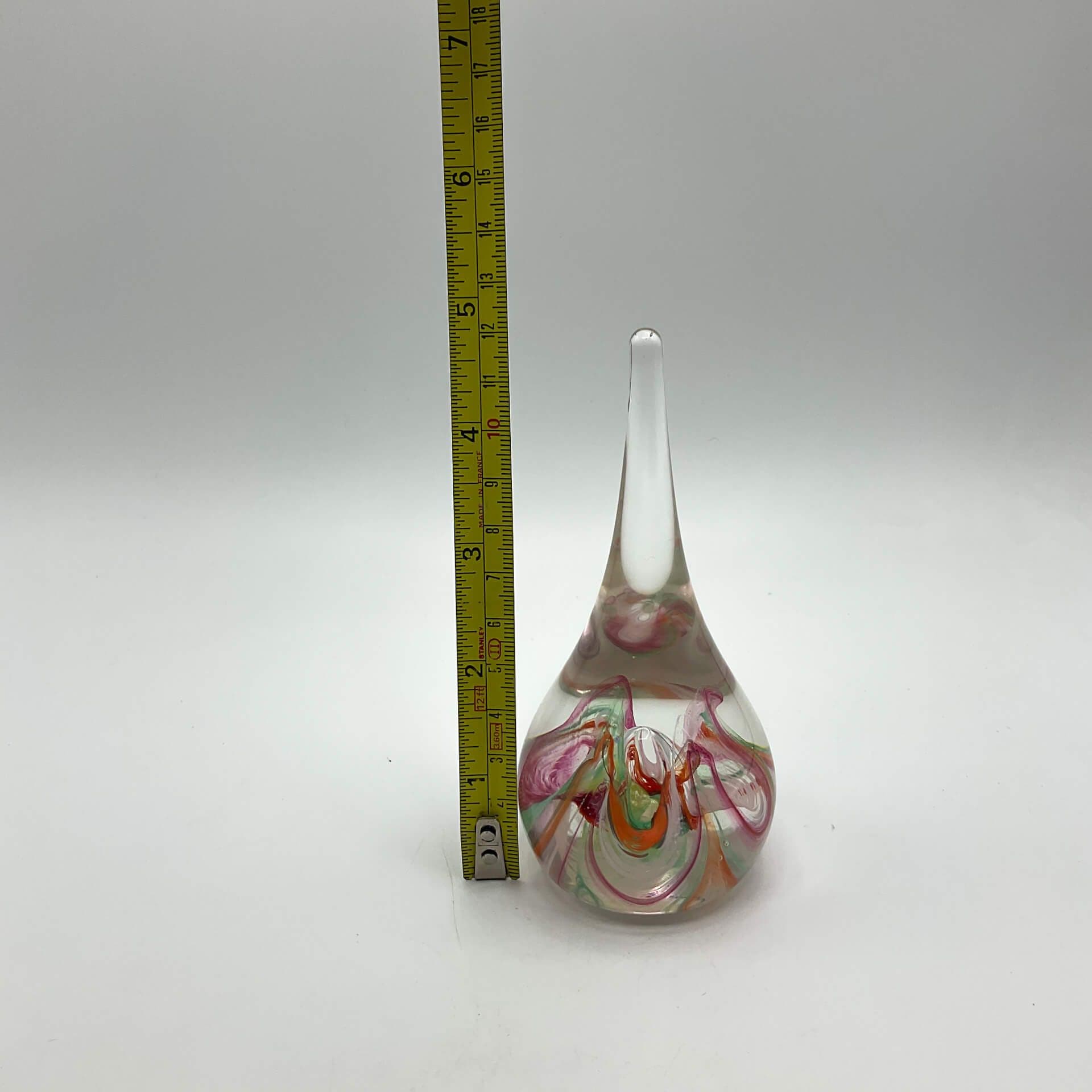 Selkirk glass paperweighrt with multicoloured swirls on a white background next to a tape measure showing the height asc just under v5 inches.