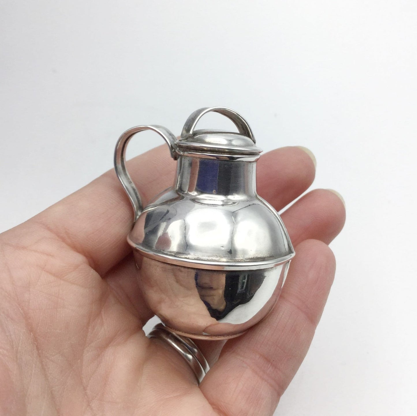 silver plated jug urn held in a hand on a plain background