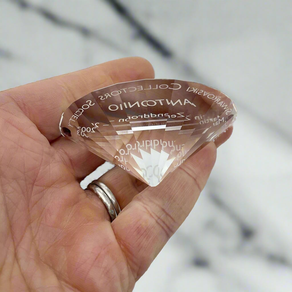 back view of crystal ornament held in a hand with a marble worktop in the background