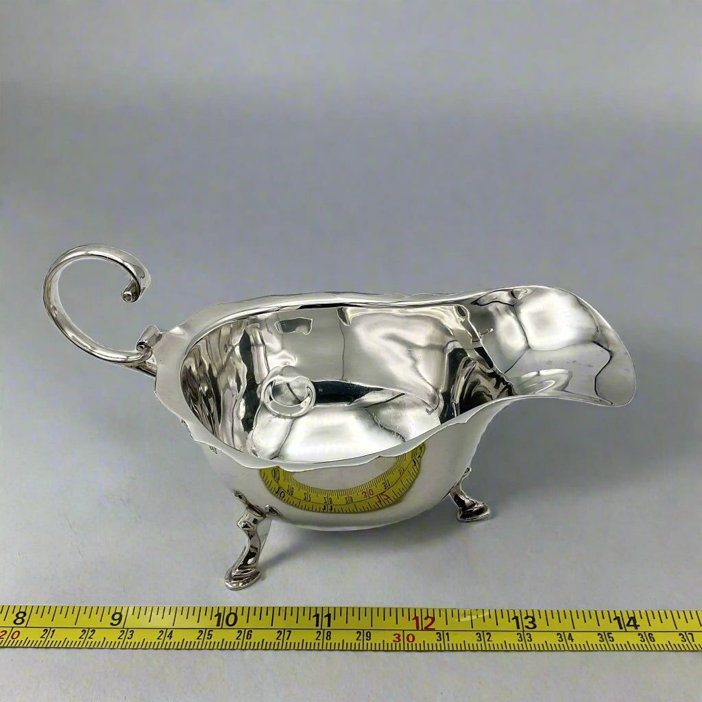 silver gravy boat with a tape measure to show the size of it on a light background