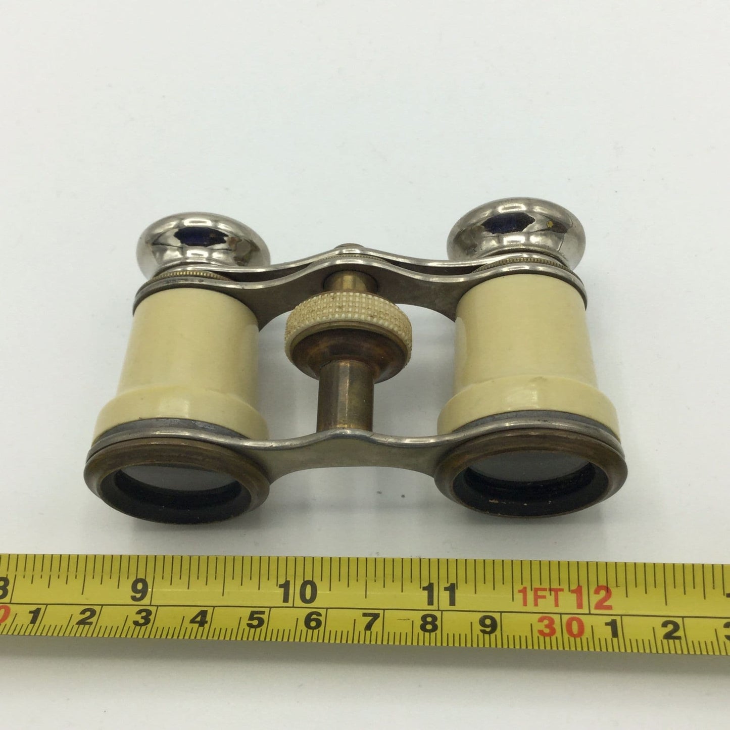 Opera glasses next to a tape measure for scale on a white background