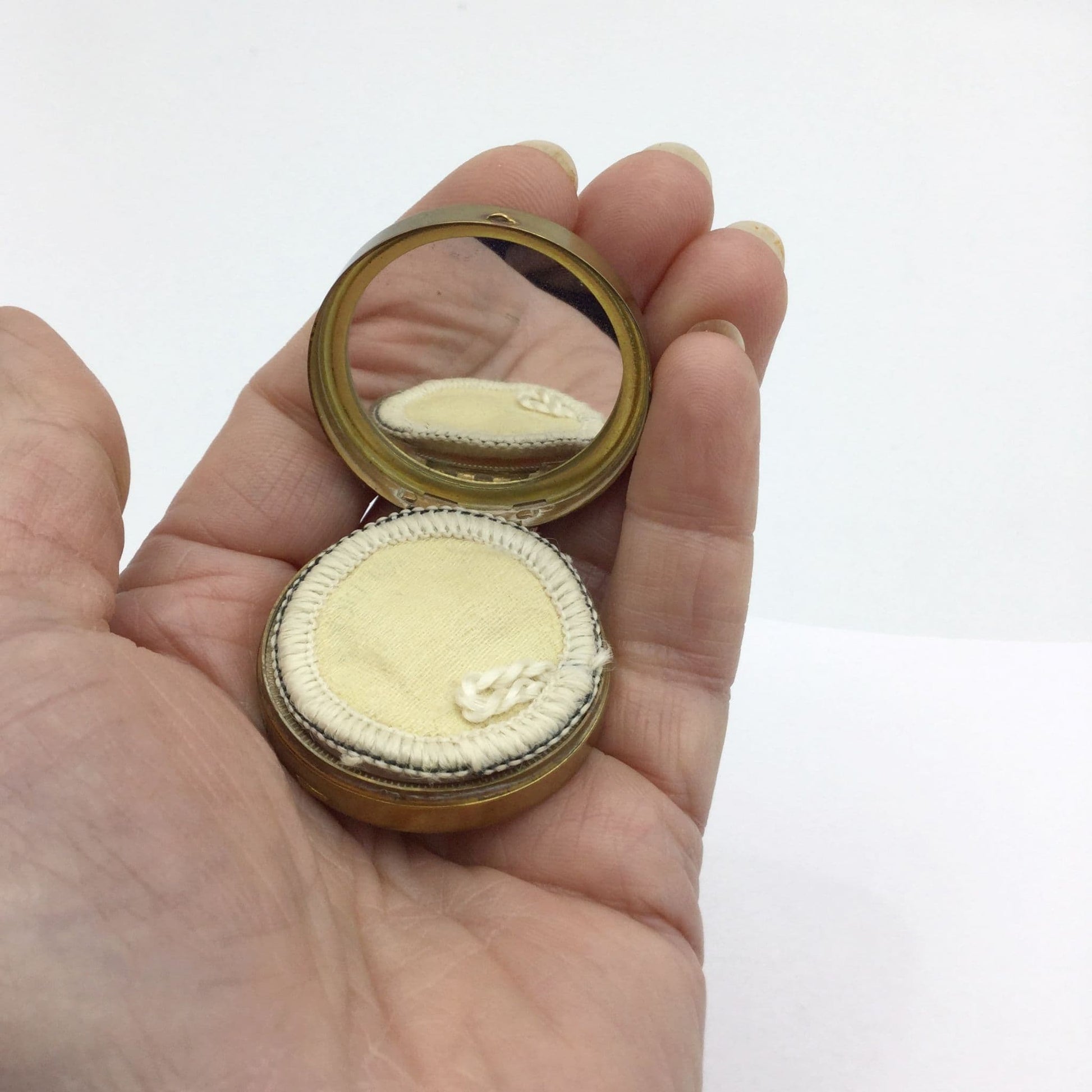 small powder compact showing a clear mirror and an unused applicator held in a hand