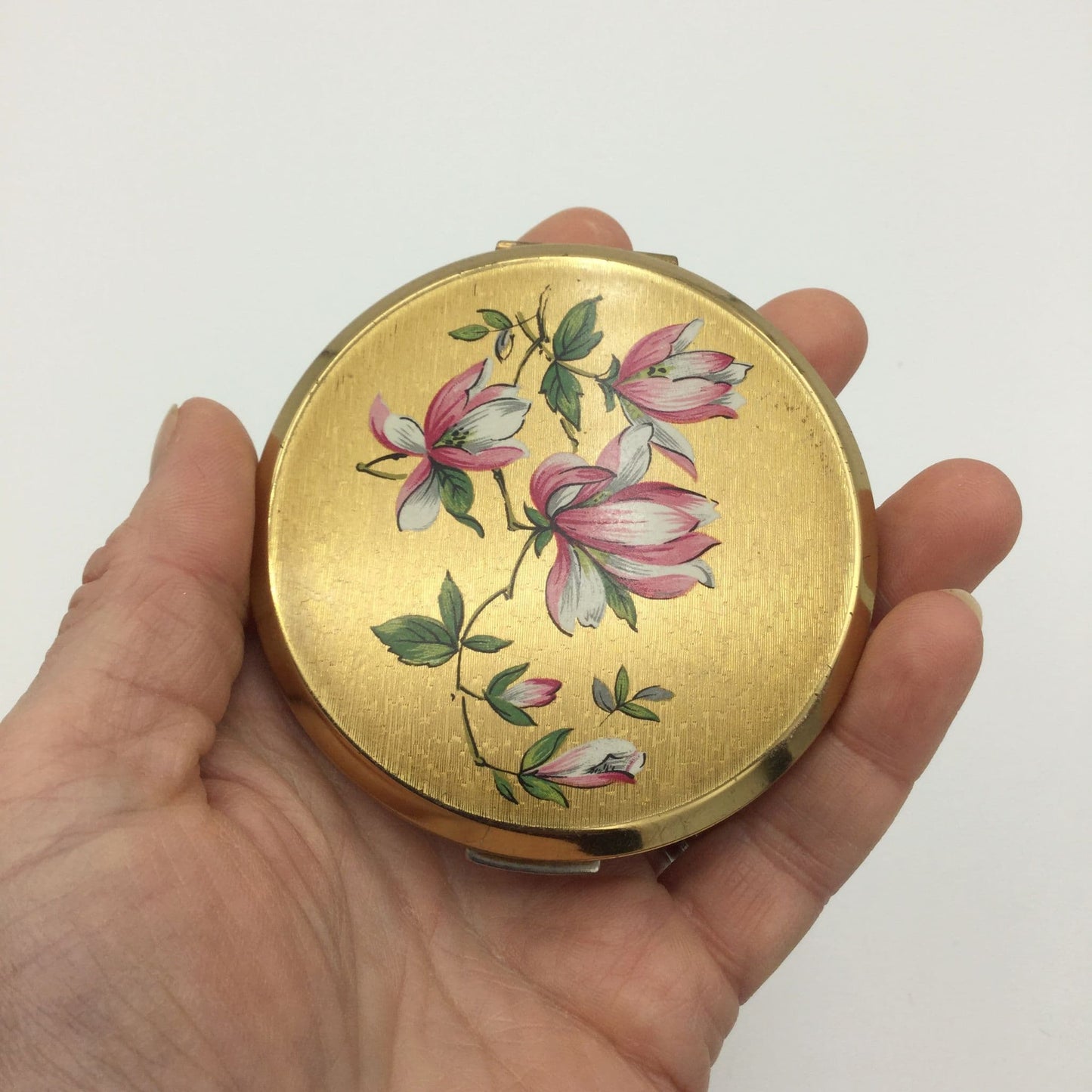 pretty gold compact with flowers on lid held in a hand
