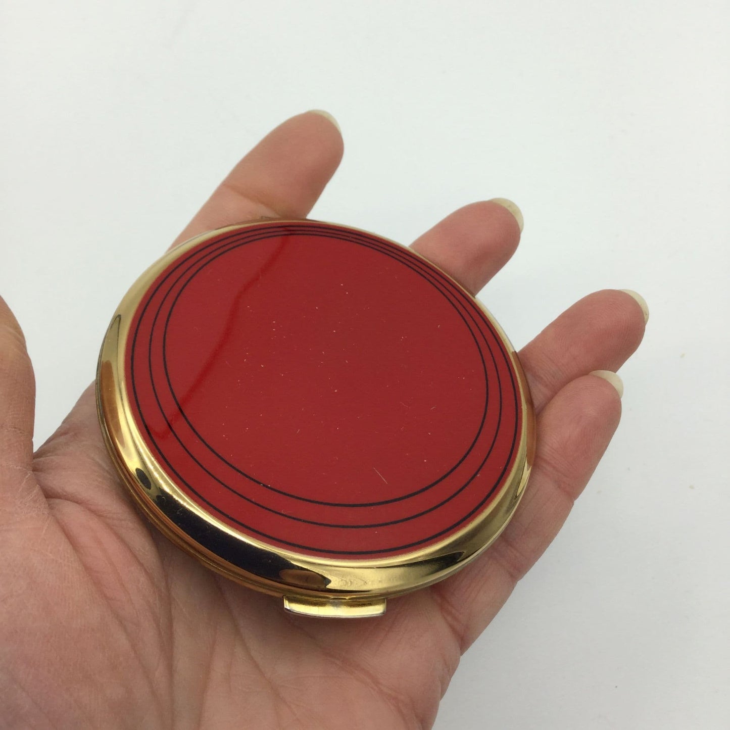 bright red powder compact with gold sides held in a hand