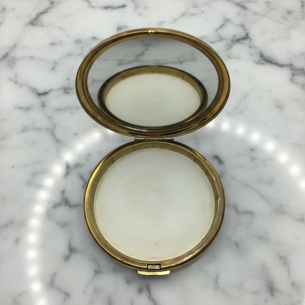Gold edged compact with a clear mirror open on a marble background