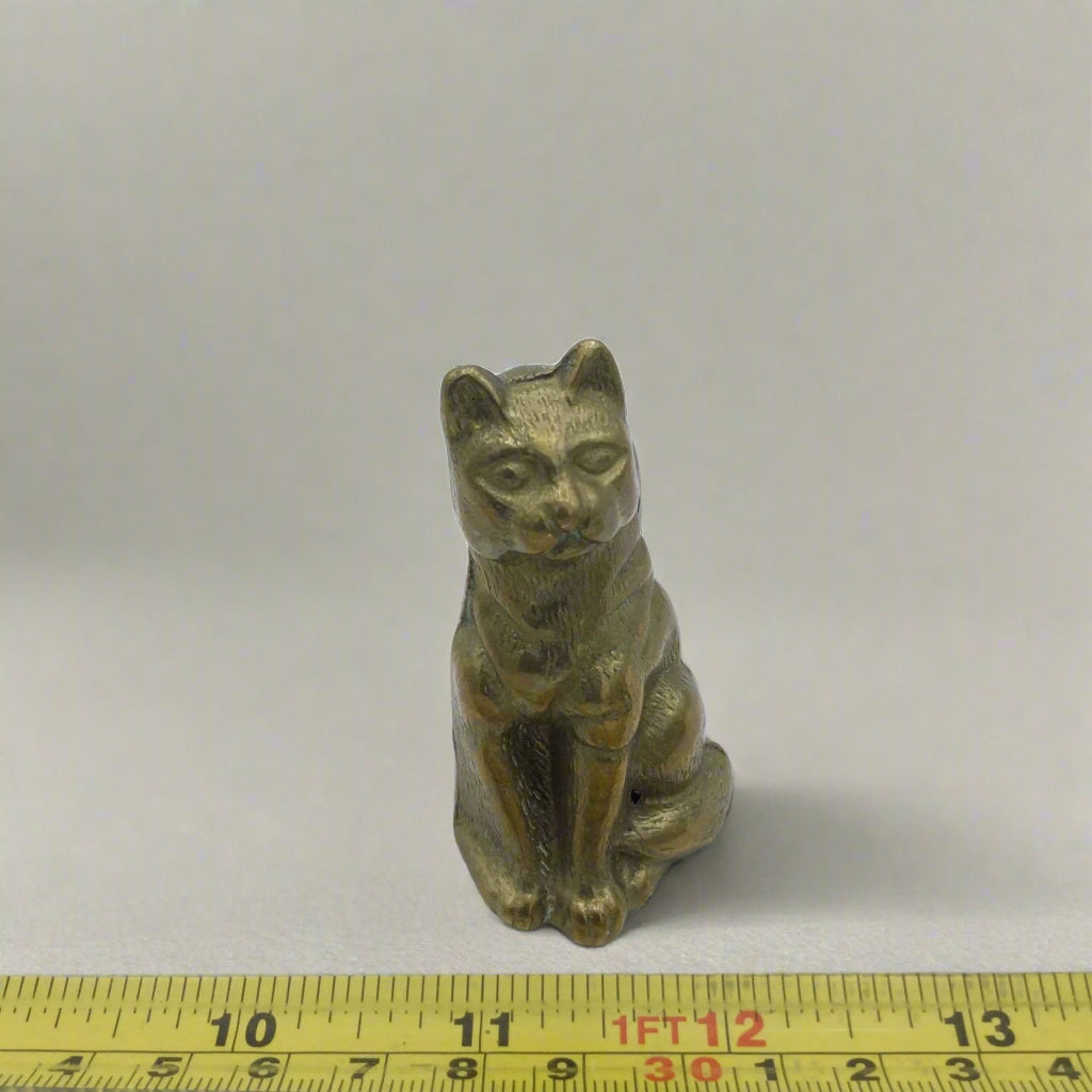 Small bronze cat figurine on a white background with a ruler for scale.