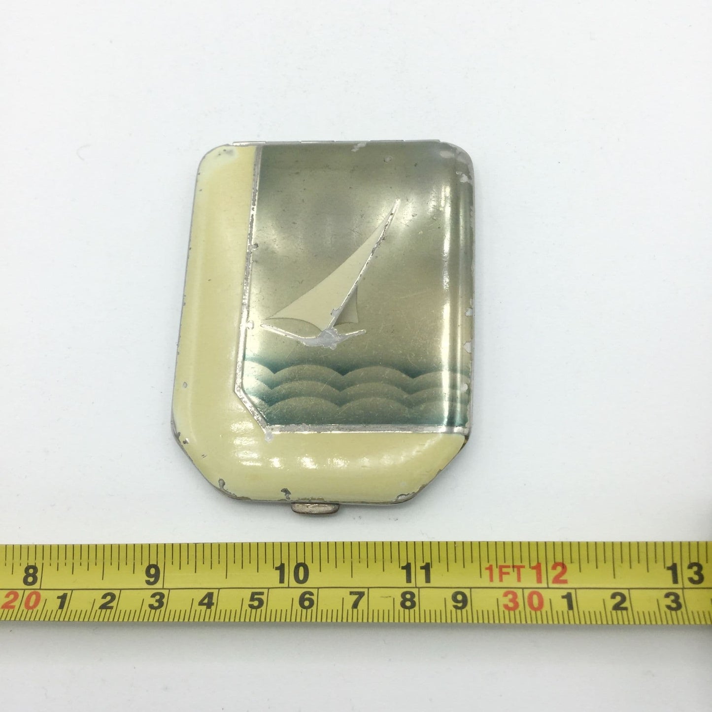 1930s art deco compact next to a tape measure showing it's width as 6cm