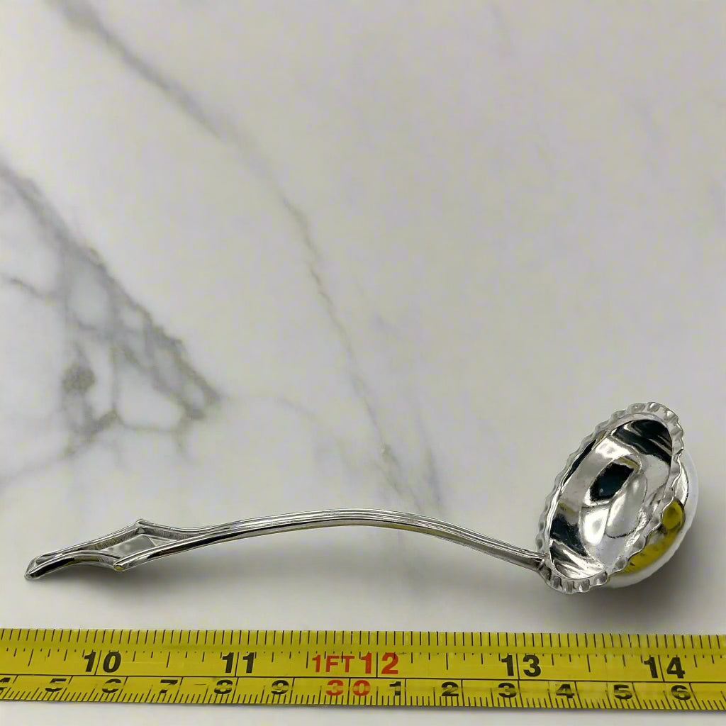 Silver ladle on a marble surface with a measuring tape for scale