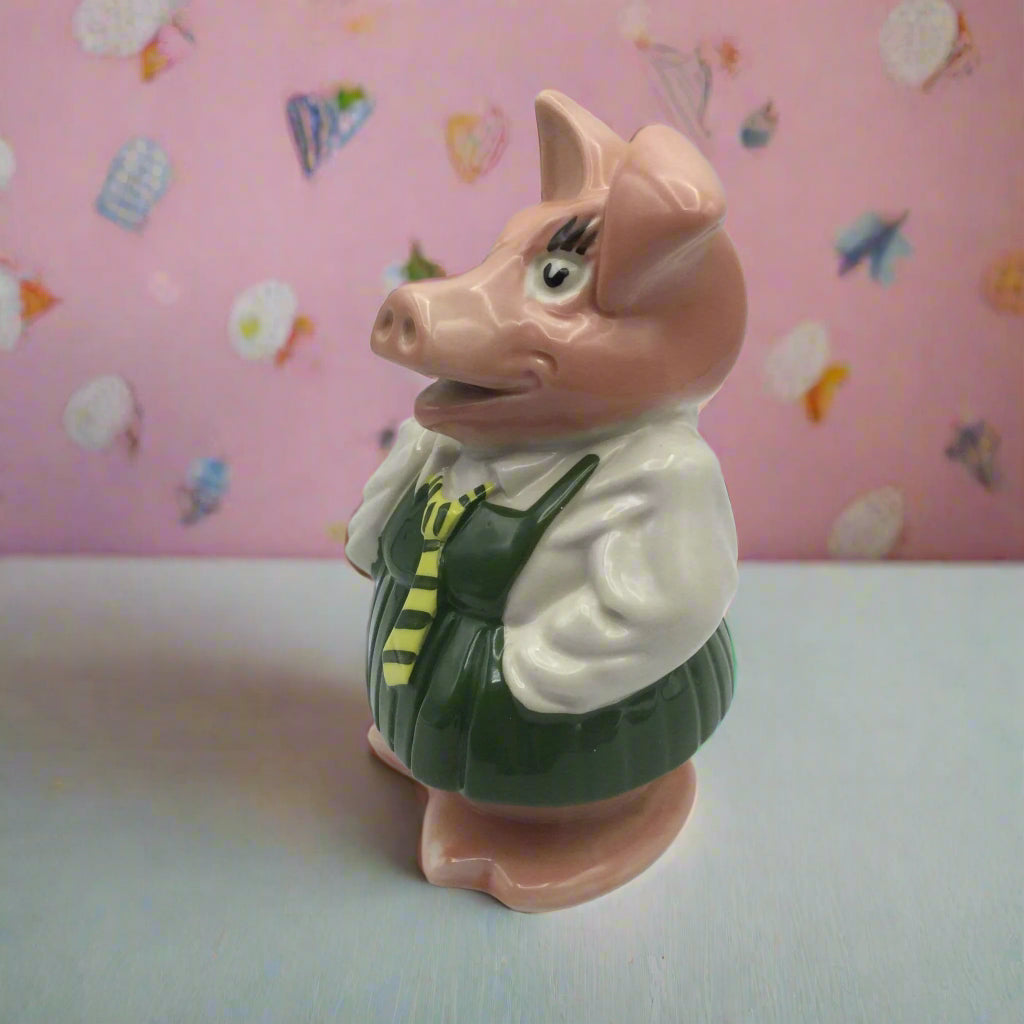 Pig figurine with a green outfit against a pink wallpaper with ice cream cone pattern