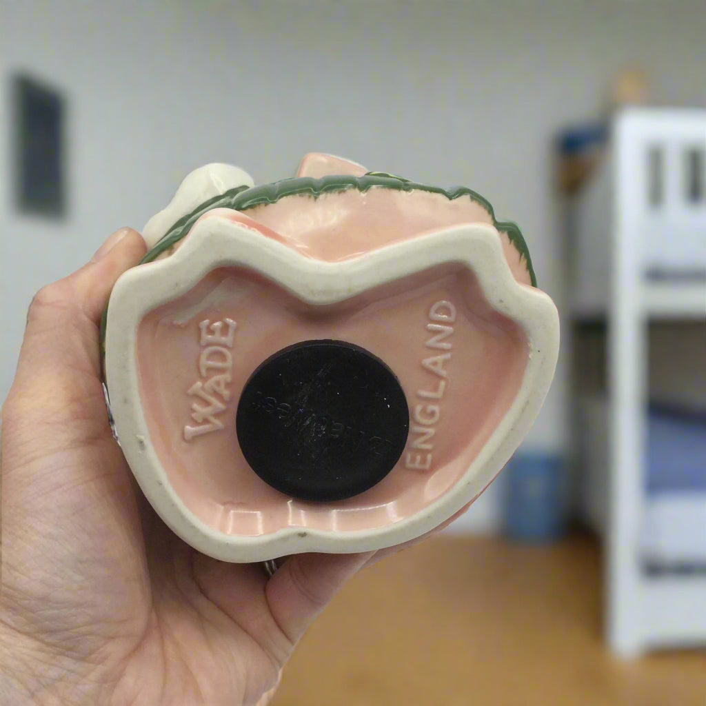 Base of Annabel Piggy Bank witth Wade England imprinted, held in a hand with a child's bedroom in the background.