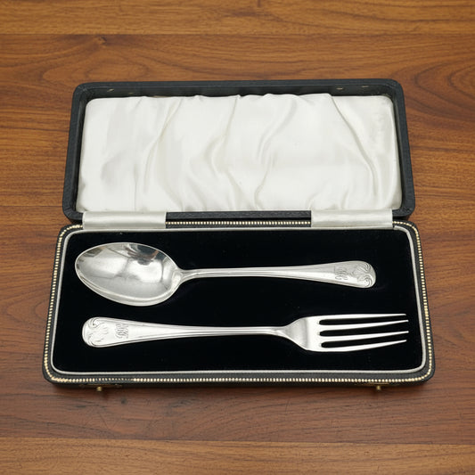 A matching silver spoon and fork sitting in a black presentation box on wood table