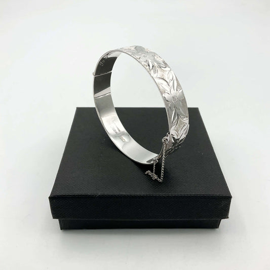 Silver bracelet with engraved flowers sitting on a black box