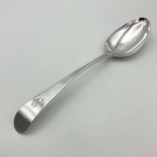 Antique silver serving spoon with an L engraved on the handle on a white background