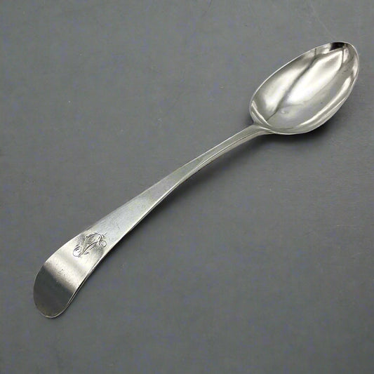Antique silver serving spoon with an L engraved on the handle on a grey background