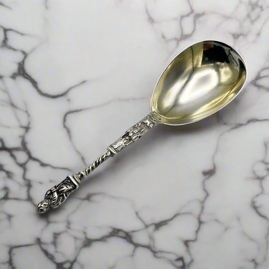 Antique sterling silver caddy spoon with a gilded bowl and an engraved handle featuring an apostle figure, possibly by Henry Holland, hallmarked in 1867 on a marble surface.