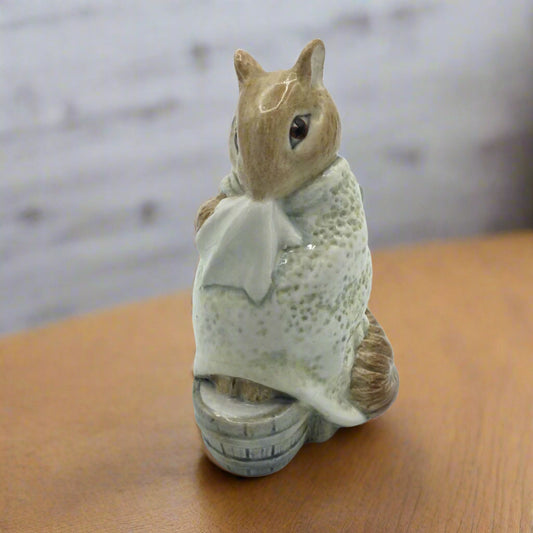 Ceramic squirrel figurine holding a white flower on a wooden surface with a blurred background