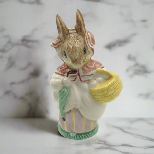 A Beswick figurine of Mrs Rabbit from the Peter Rabbit stories, carrying a green umbrella and a yellow basket, dressed in a pink and white outfit.