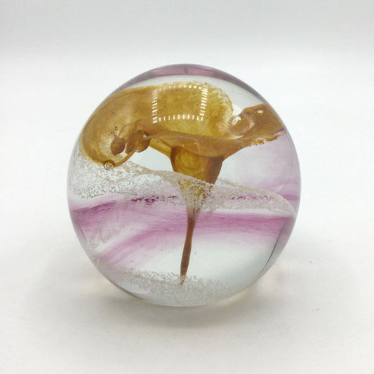 Glass paperweight with a gold and pink design on a white background