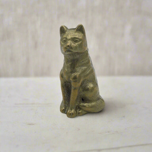 A vintage brass cat figurine sitting with a curled tail, showing detailed brass craftsmanship.
