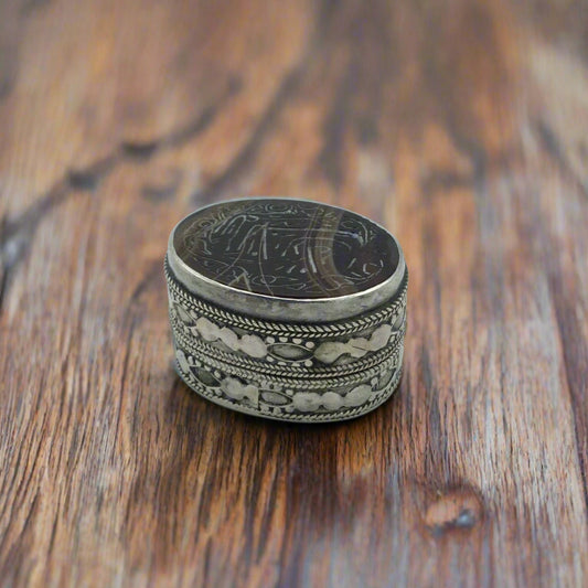 Decorative silver ring with intricate designs on a wooden surface