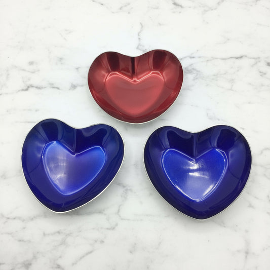 three heart shaped enamel bowls on a marble surface