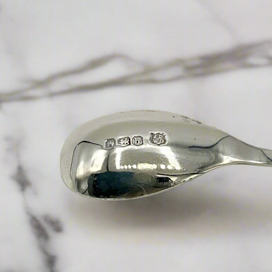 The back of a spoon showing silver maker’s marks and hallmarks with a marble surface background 