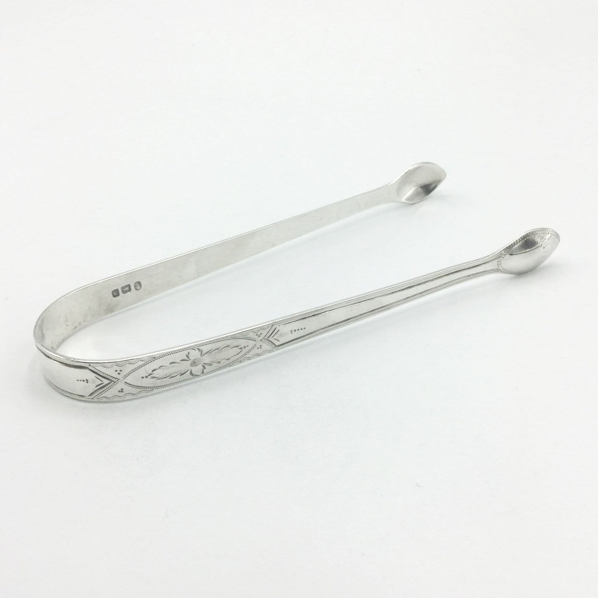 1700s Silver sugar tongs with a pretty floral engraved design on a white background