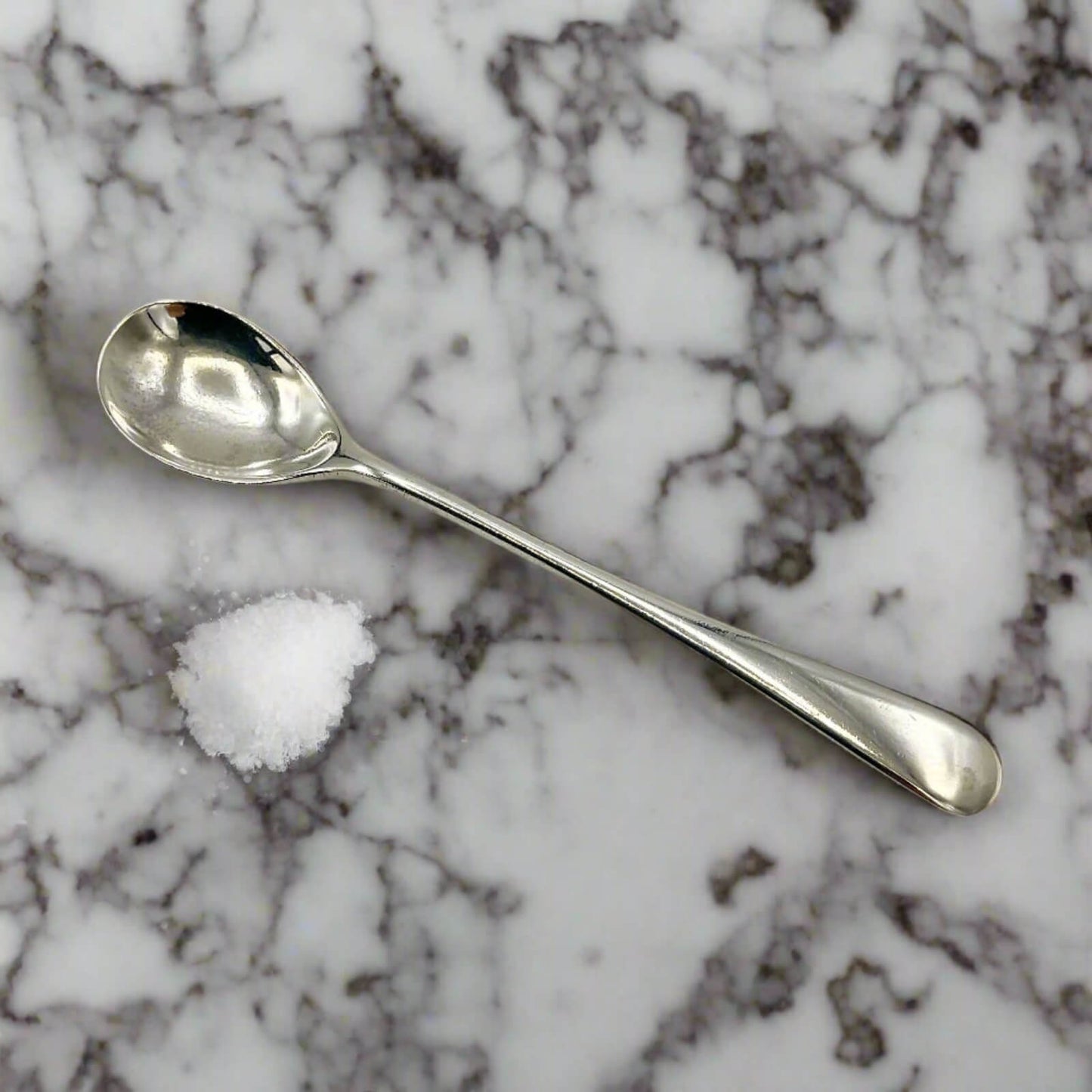 Silver spoon and small pile of salt on a marble surface