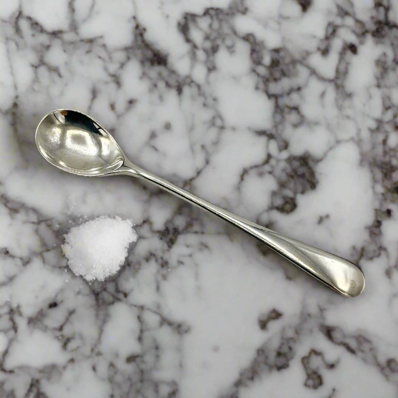 Silver spoon and small pile of salt on a marble surface
