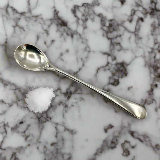 Silver spoon and small pile of salt on a marble surface