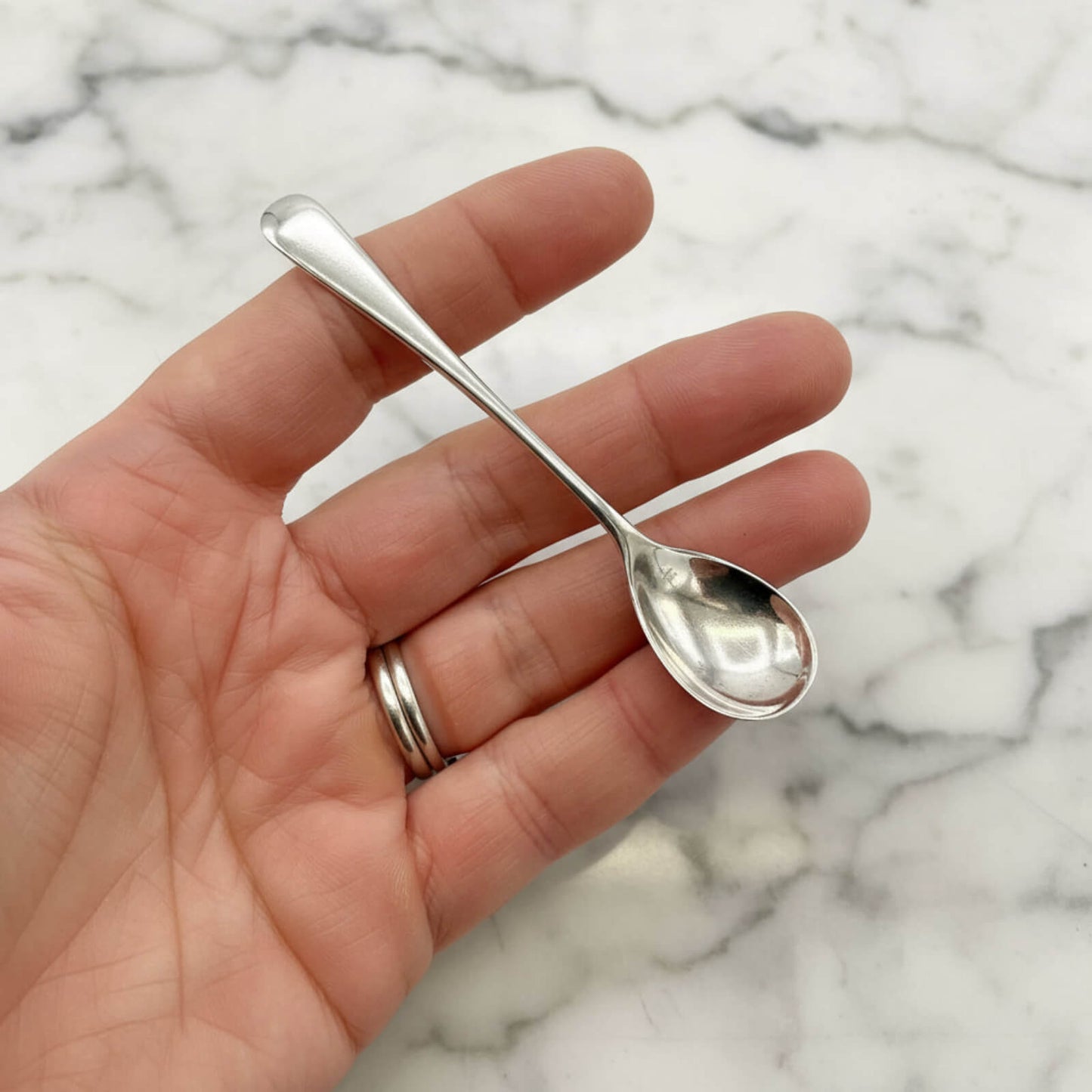 Small silver spoon held in a hand against a marble background
