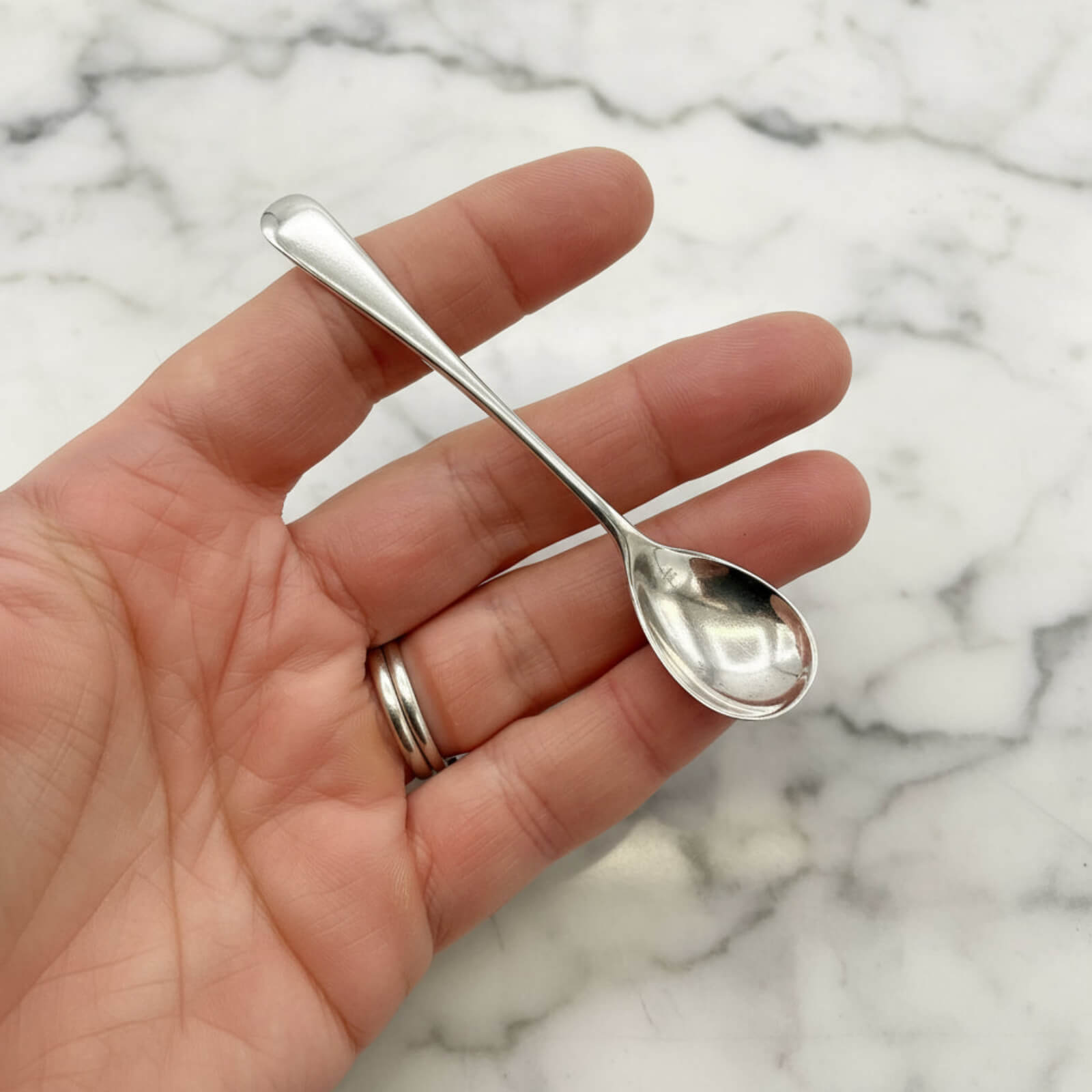 Small silver spoon held in a hand against a marble background