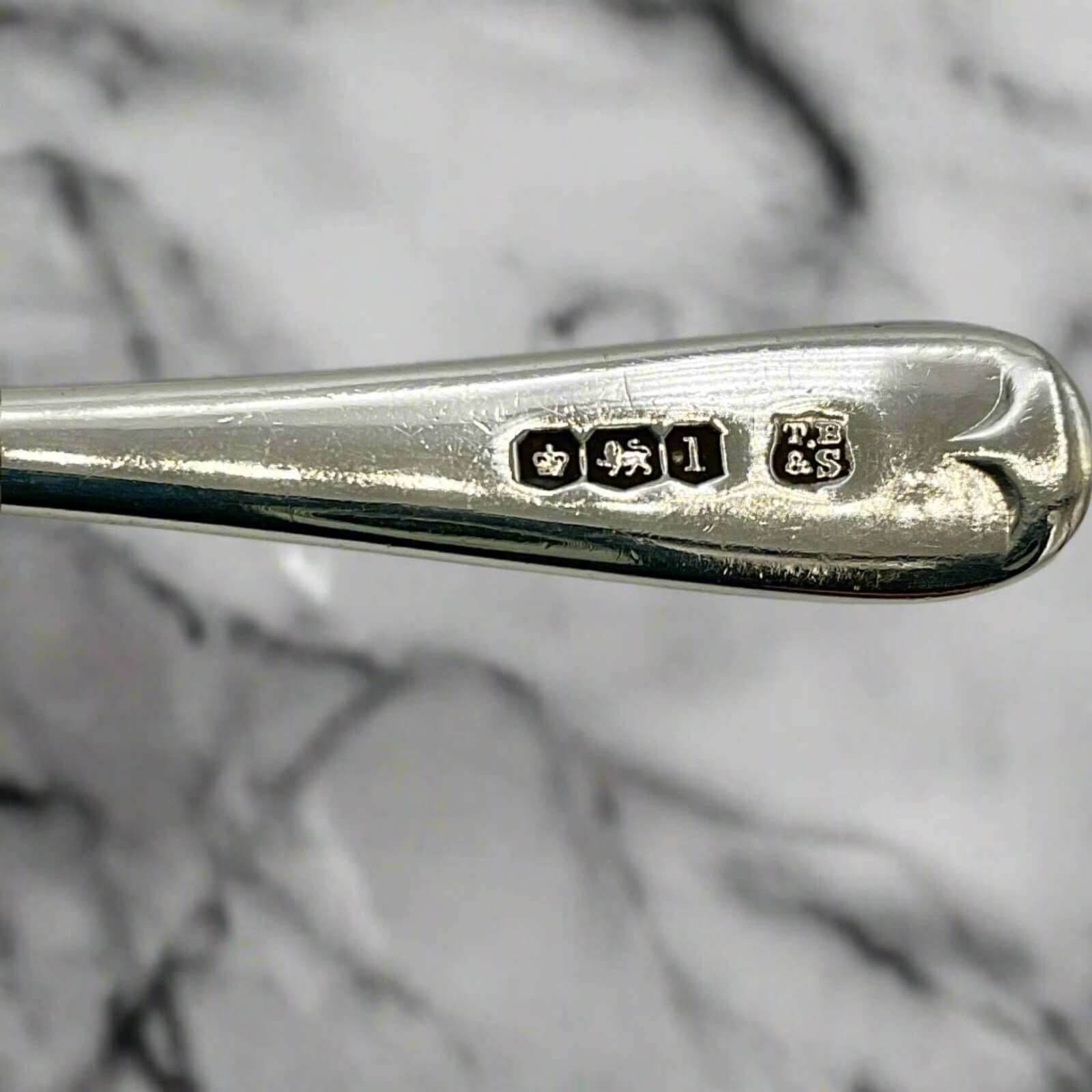 Close-up of a silver spoon with engraved hallmarks on a marble surface