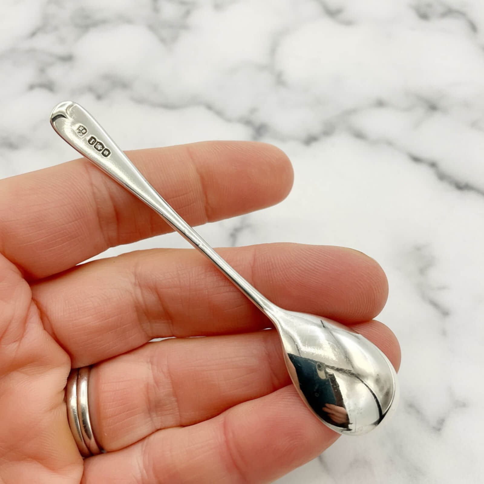 Silver spoon held in a hand with a marble background