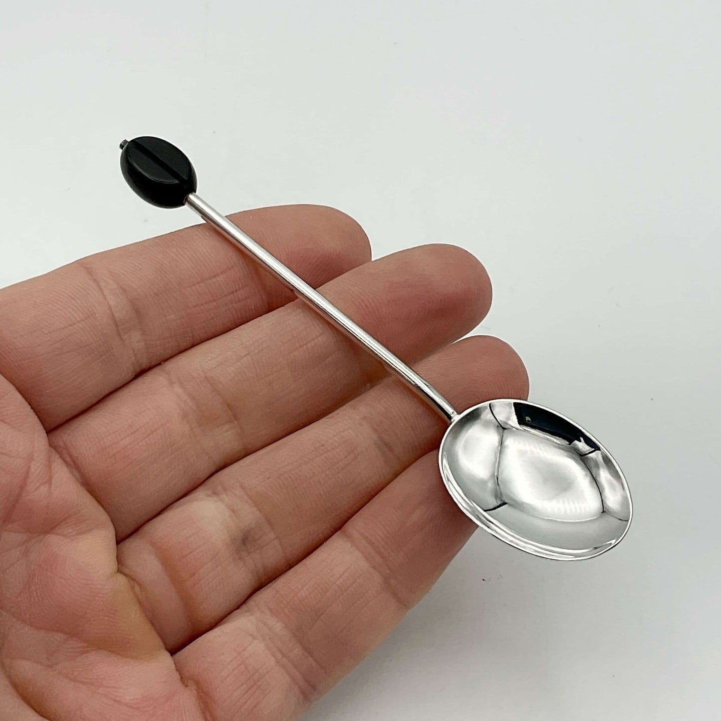 A beautiful silver coffee spoon with coffee bean finial held in a hand