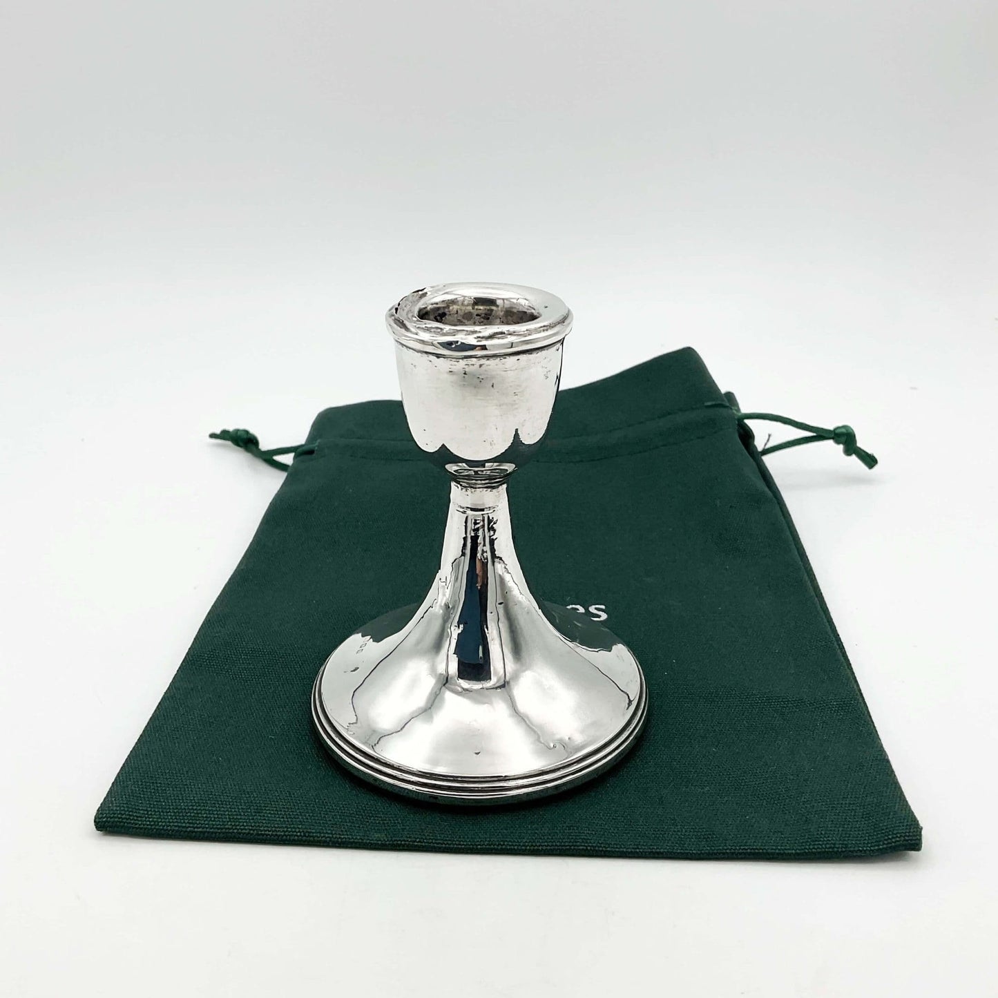 A single silver candlestick sitting on a green cotton bag